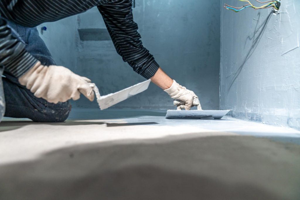 Construction worker applying wall putty with spatula home renovation repair plastering tools blue wall background