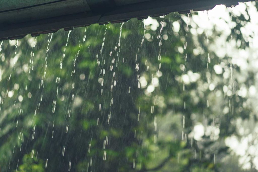 Rain drops falling from roof with blurred green nature background bokeh effect